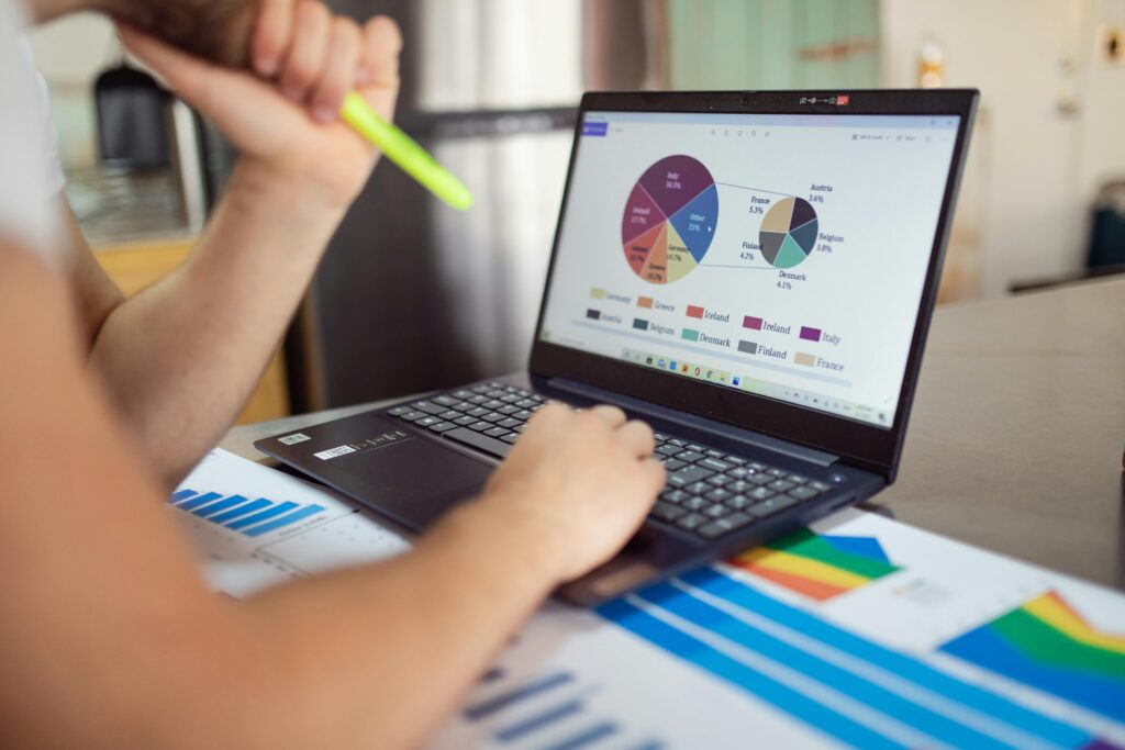 pexels-photo-7948060-7948060 Person analyzing financial charts and graphs on a laptop with colorful documents, showcasing market analysis.